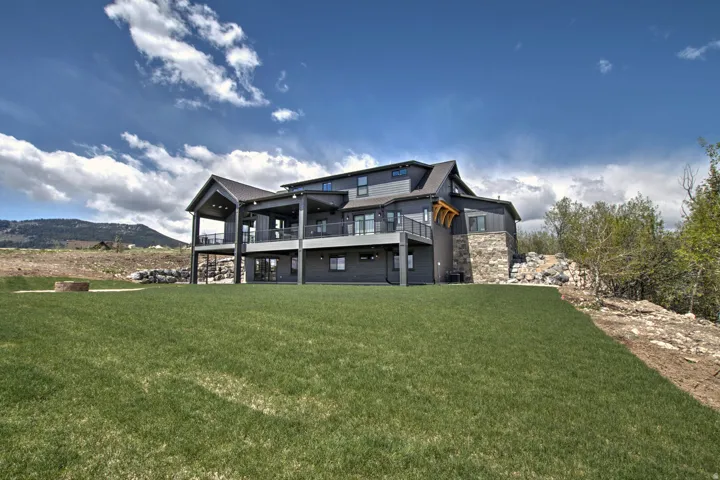 Modern multi-level exterior featuring dark siding, stone accents, multiple covered balconies with dark railings, and a lower-level patio with sliding glass doors