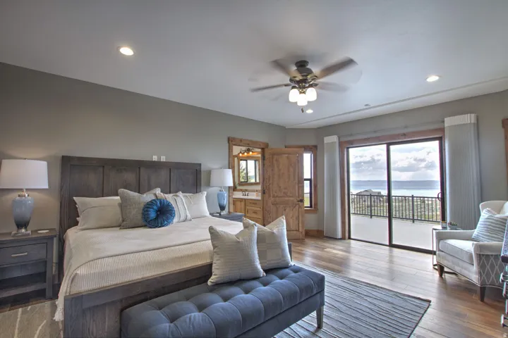 Spacious room featuring wood-finish flooring, a ceiling fan with integrated lighting, recessed lighting, and a private balcony with sliding glass doors overlooking a water and landscape setting