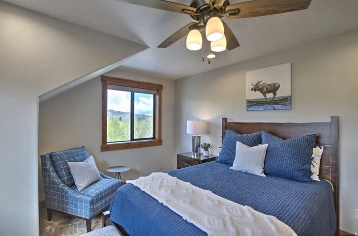 Bedroom featuring a wood-frame window with exterior scenery, a ceiling fan with integrated lighting, wood-finish flooring, and a built-in angled wall