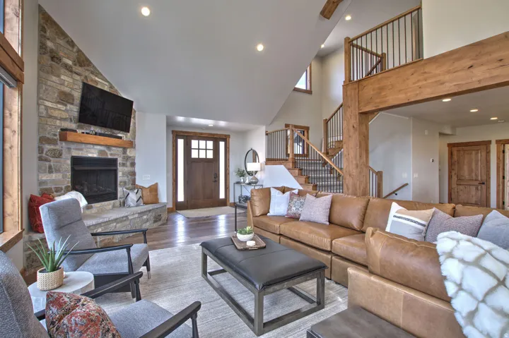 Spacious living area featuring a stone fireplace with a wood mantle, high ceilings, wood-finish flooring, and a prominent staircase with iron balusters