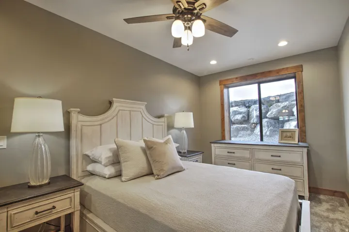 Bedroom featuring a large window with a natural rock backdrop, a wood-finish ceiling fan with integrated lighting, and recessed ceiling lights