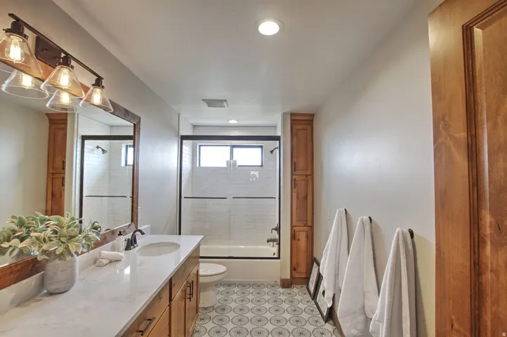 Bathroom featuring a wood-finish vanity with an undermount sink and light-toned countertop, a framed mirror, and a multi-bulb vanity light fixture
