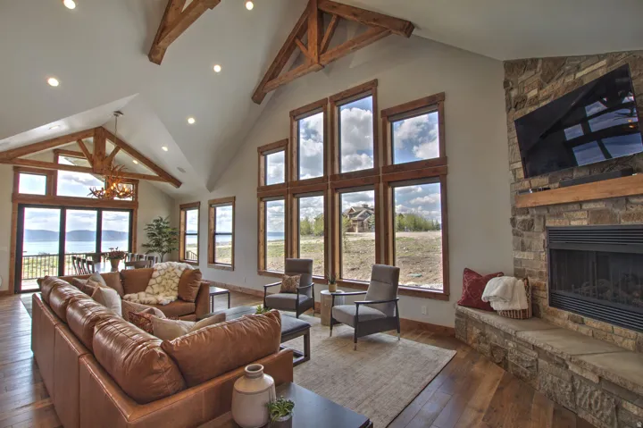Spacious living area featuring exposed wood beams, a vaulted ceiling with recessed lighting, and expansive windows