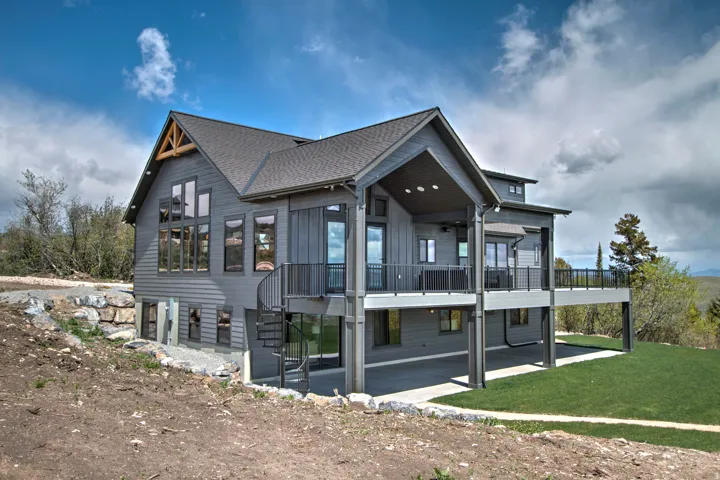 Multi-level residential structure featuring gray siding, a prominent gable roof with exposed timber trusses, and extensive glazing