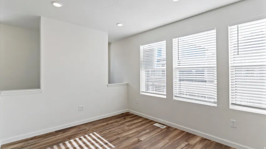 Room featuring wood-finish flooring, three windows with white blinds, recessed lighting, and white walls with built-in wall niches