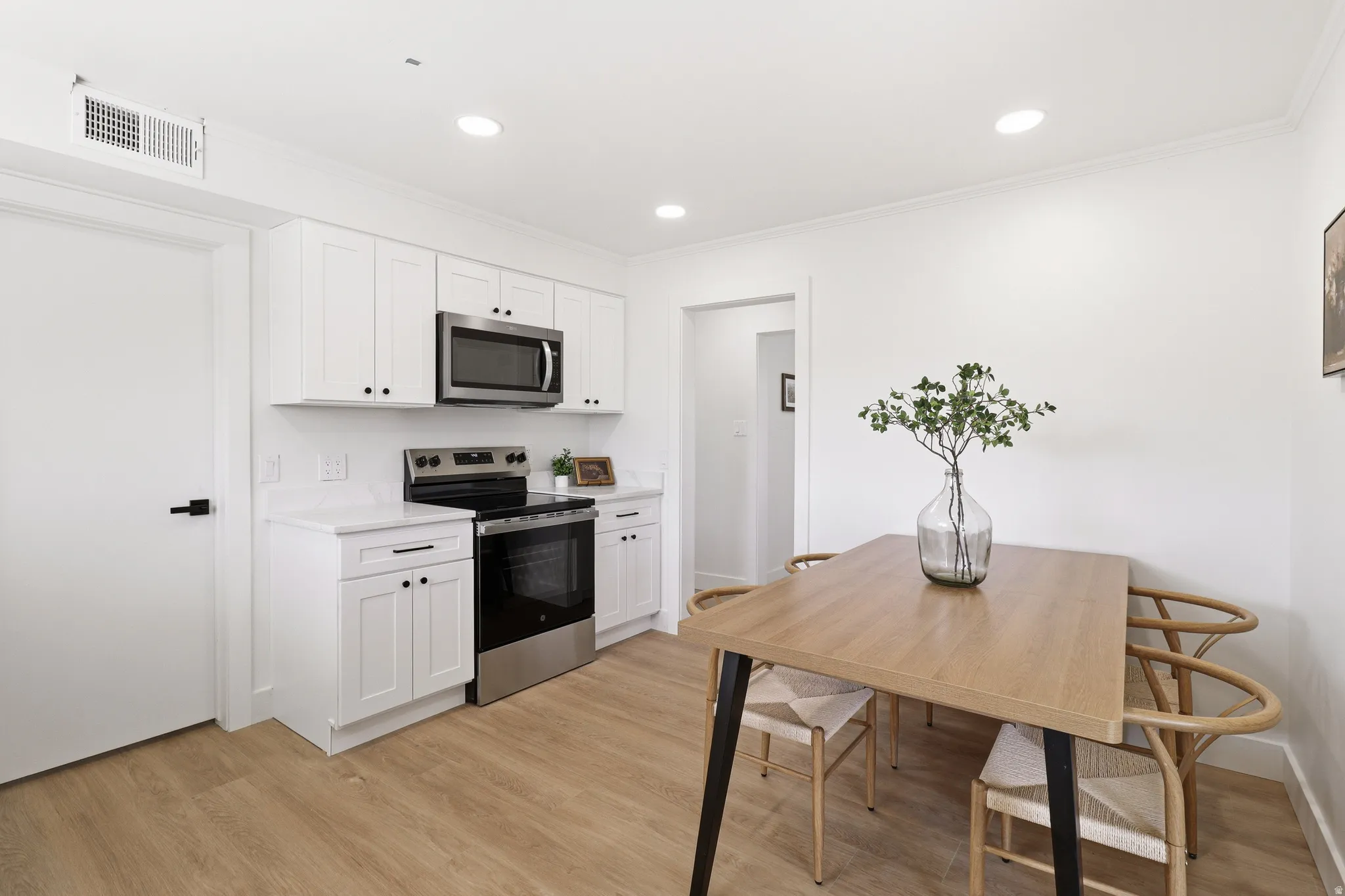 Well-appointed kitchen featuring white shaker cabinetry, stainless steel appliances, white countertops, and wood-finish flooring