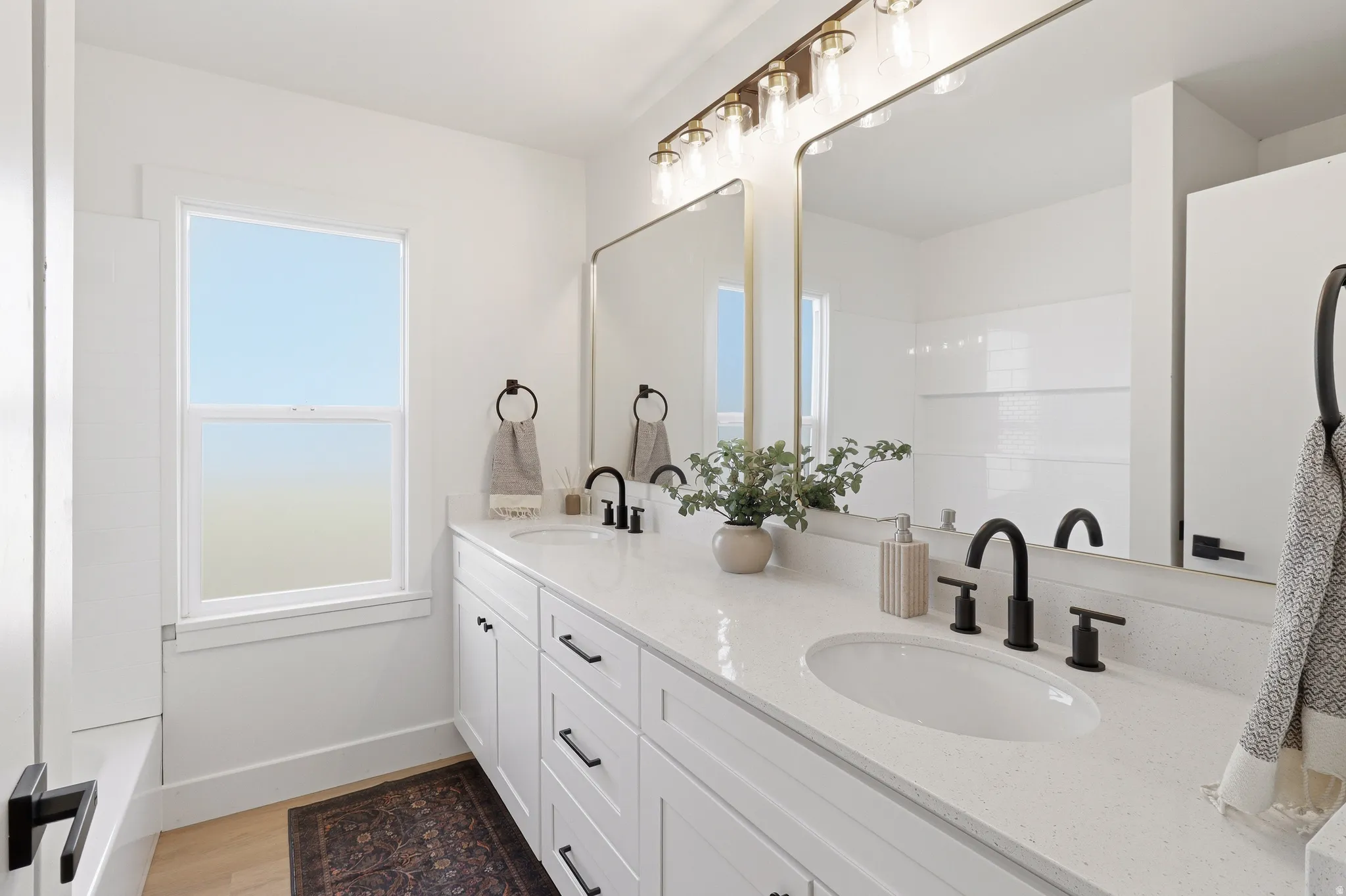 Double vanity featuring white shaker-style cabinetry, white countertops, dual undermount sinks with matte black fixtures, and a large mirror with a brass frame