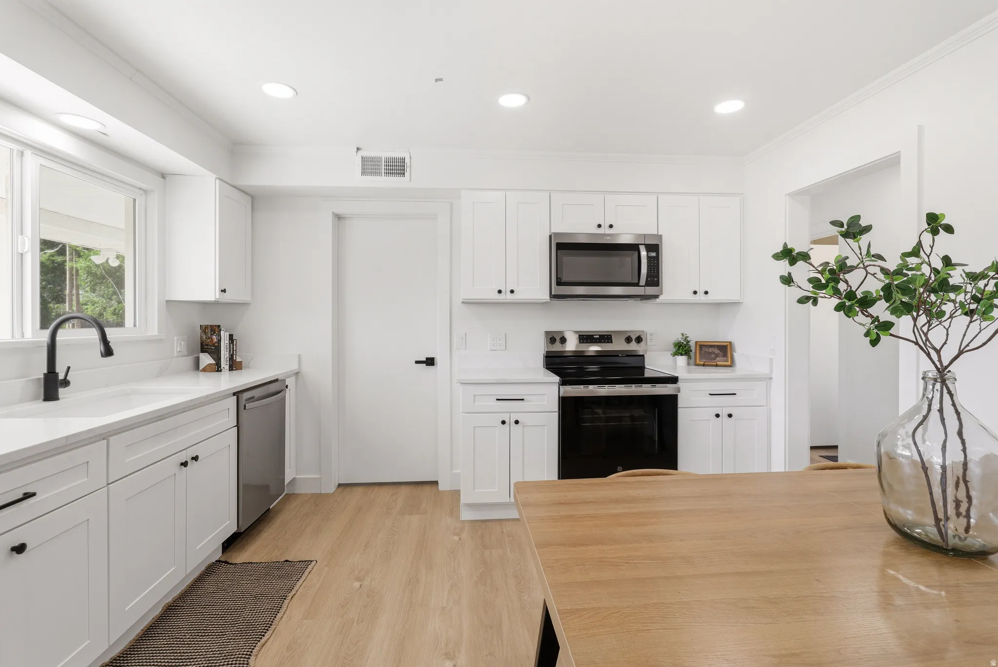Bright kitchen featuring white cabinetry, light countertops, wood-finish flooring, and recessed lighting