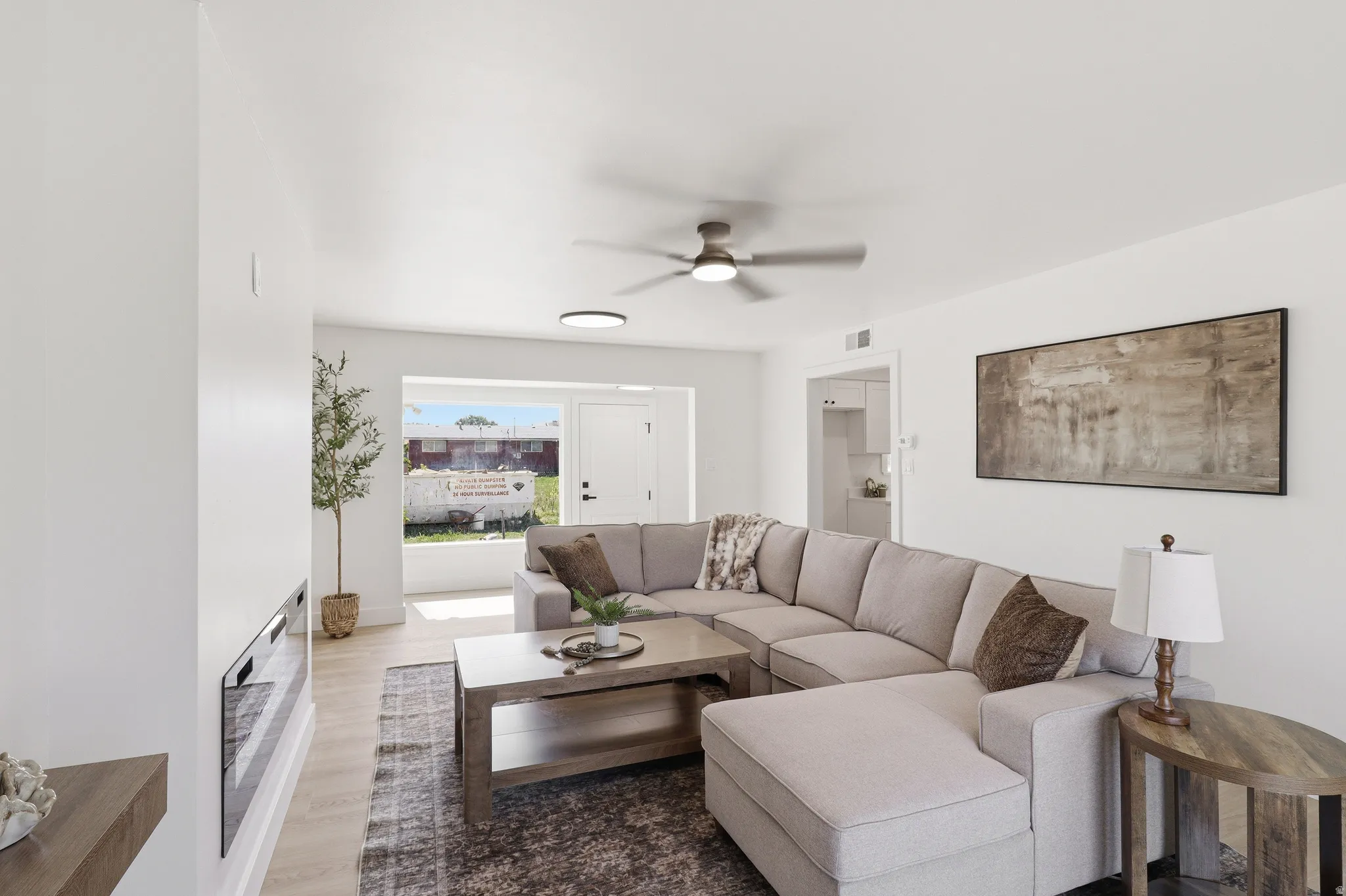 Open-concept living space with light-tone wood-finish flooring, a contemporary ceiling fan, and a wide window providing natural illumination