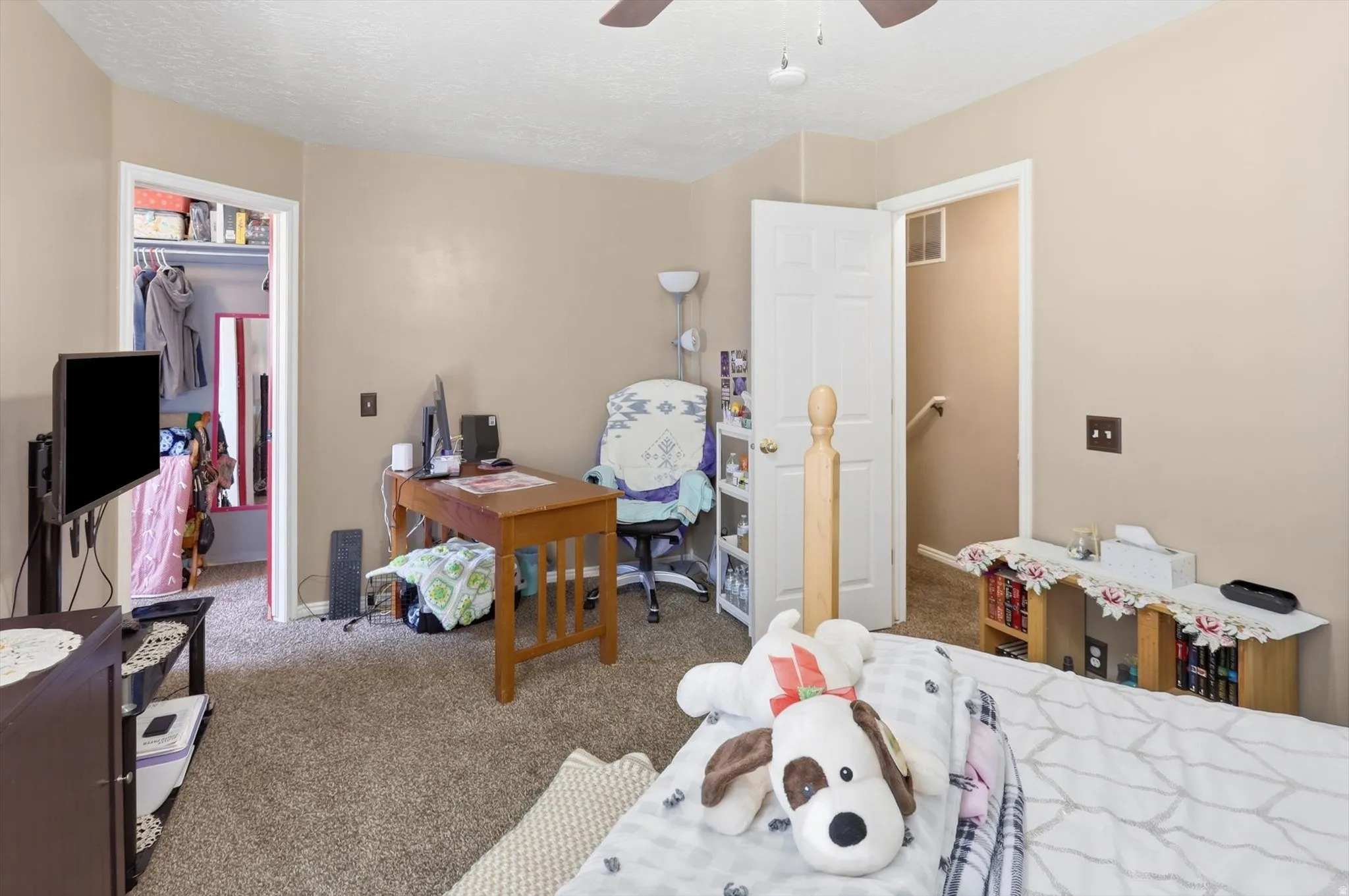 Carpeted room featuring a ceiling fan, a built-in closet with an open doorway, and a white interior door
