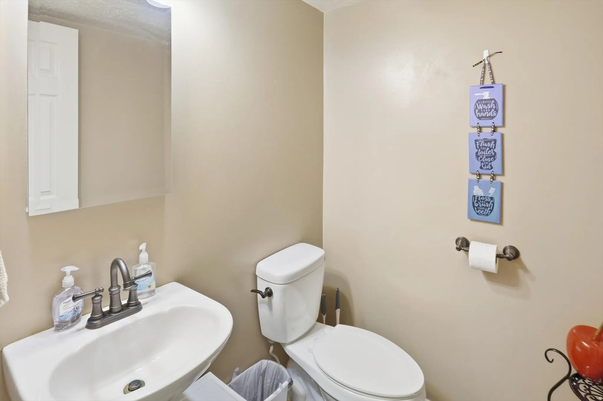 Bathroom featuring a white pedestal sink, brushed bronze faucet, wall-mounted mirror, and a white toilet
