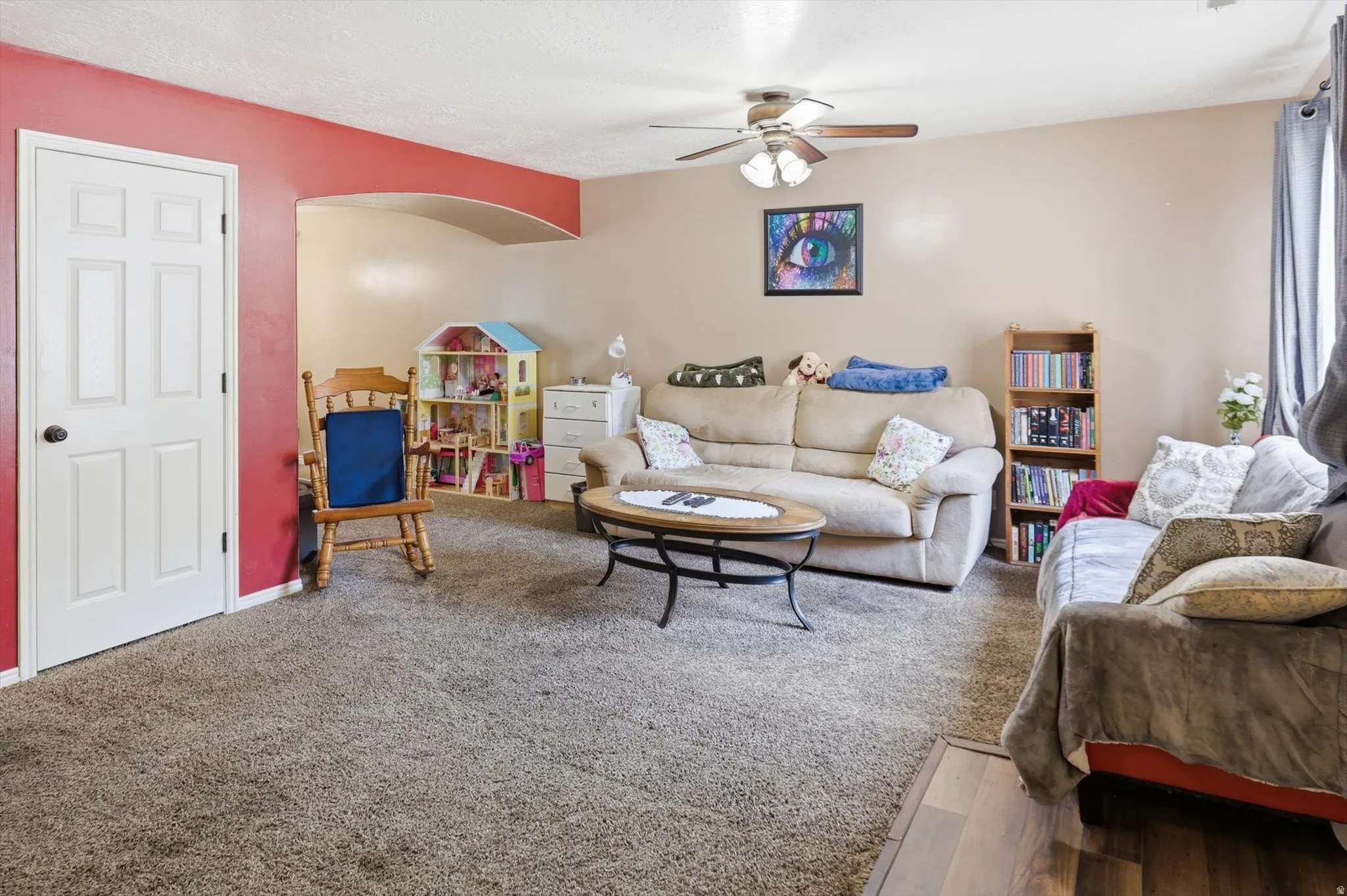 Carpeted living area featuring a ceiling fan with integrated lighting, an arched doorway, a white paneled door, and a defined section of wood-finish flooring
