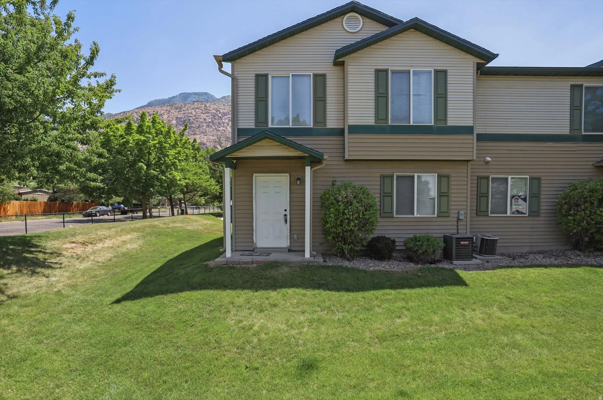 Two-story multi-unit structure with tan siding and dark green trim