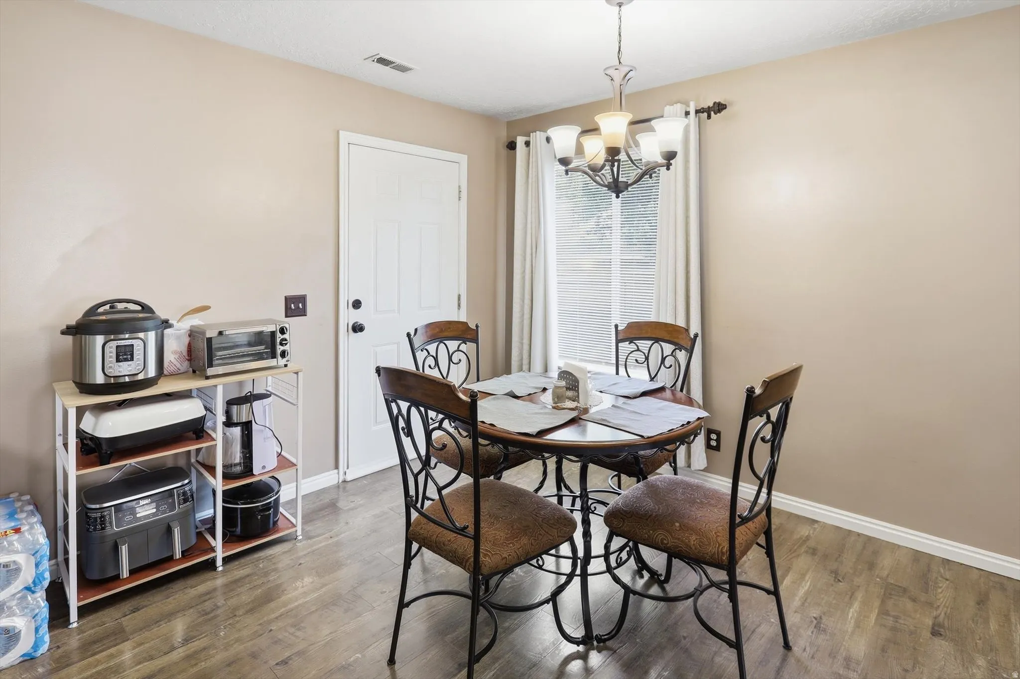 Dining area featuring wood-finish flooring, a window with blinds and curtains, a built-in light fixture, and a paneled door