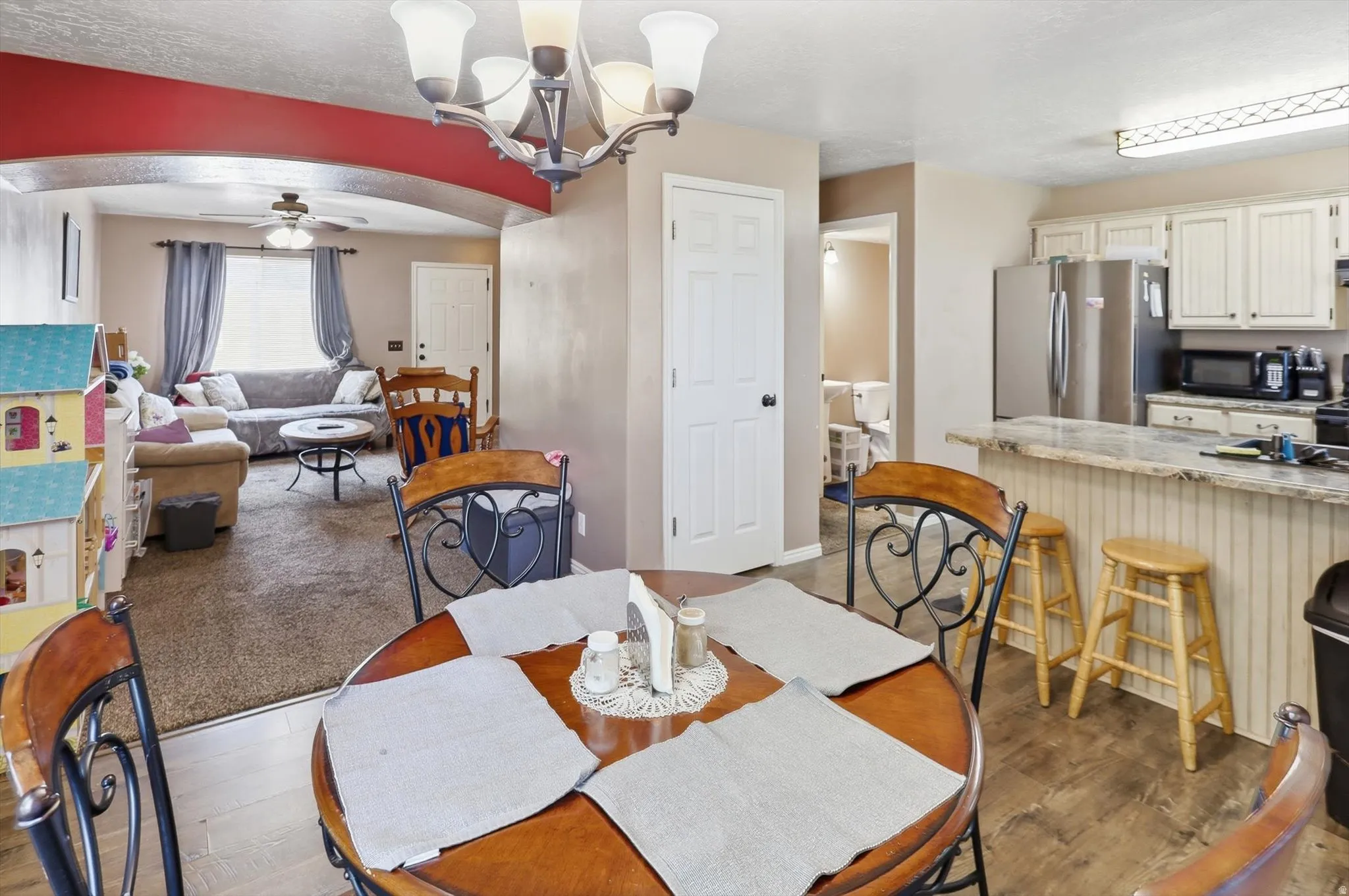 Open-concept living area featuring a breakfast bar with beadboard paneling, wood-finish flooring, and a dining area with an overhead chandelier