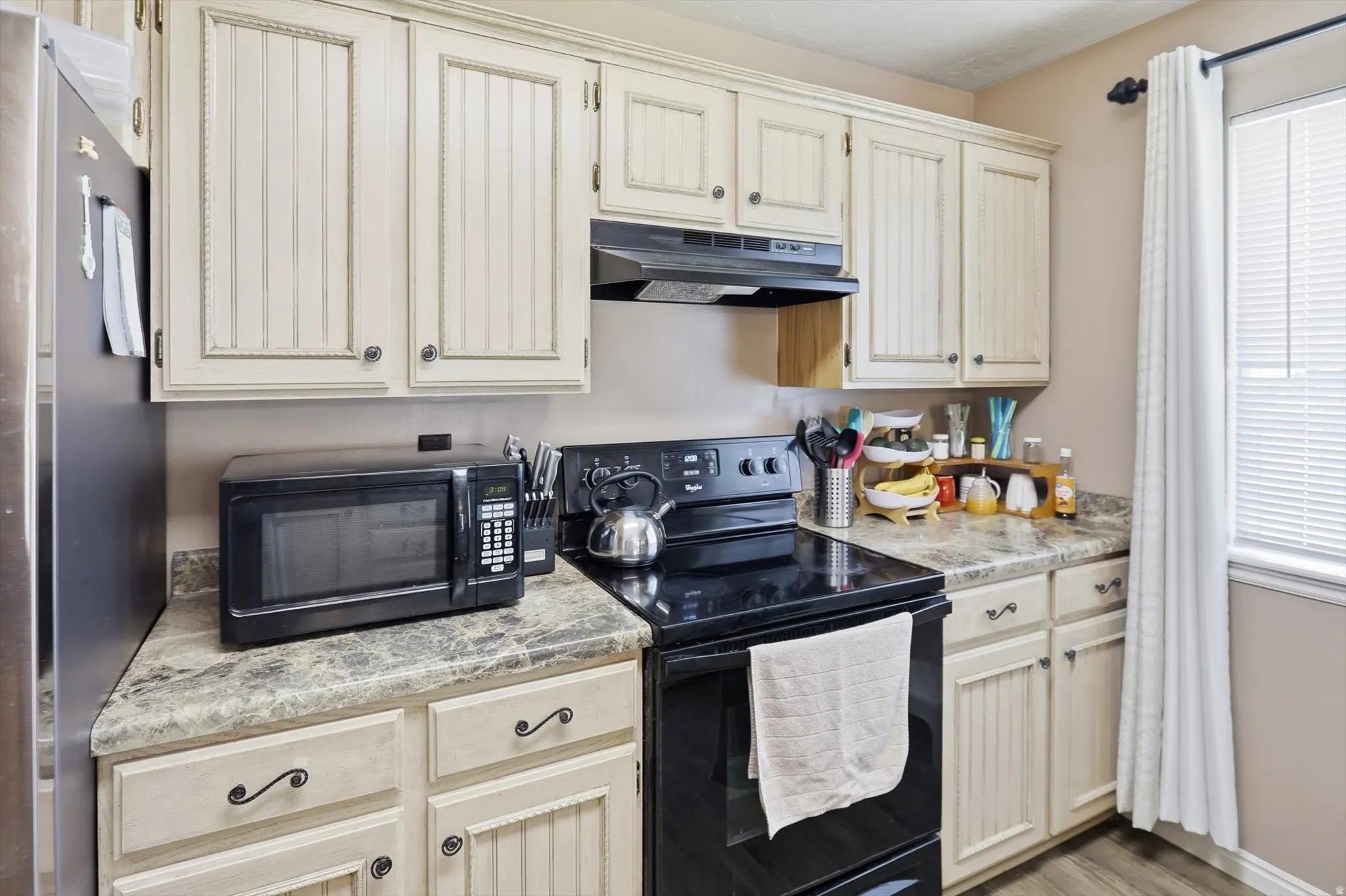 Kitchen featuring cream-colored beadboard cabinetry, dark countertops, and a black range with an overhead vent
