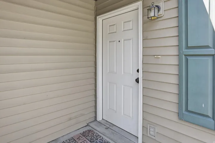 Entry with a four-panel door, tan horizontal siding, and a mounted exterior light fixture