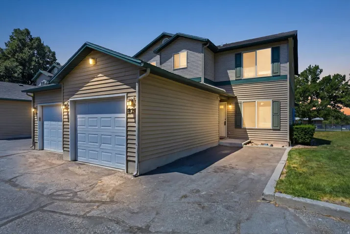Exterior featuring siding with green trim, a two-car garage with panel doors, multiple windows with dark green shutters, and a concrete driveway