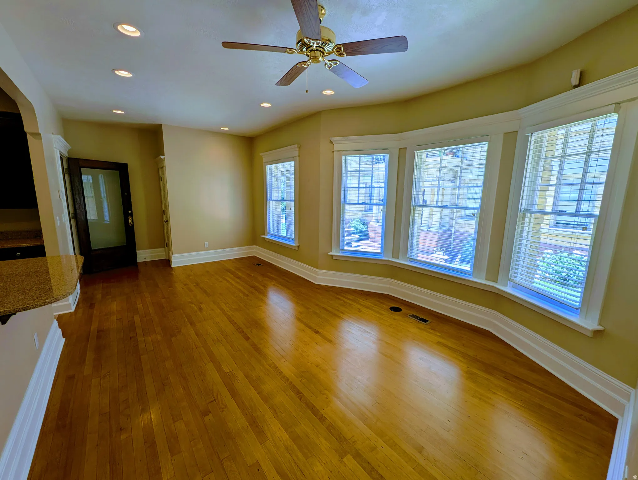 Spacious living area featuring polished wood-finish flooring, a bay window with three double-hung windows, recessed lighting, and a ceiling fan