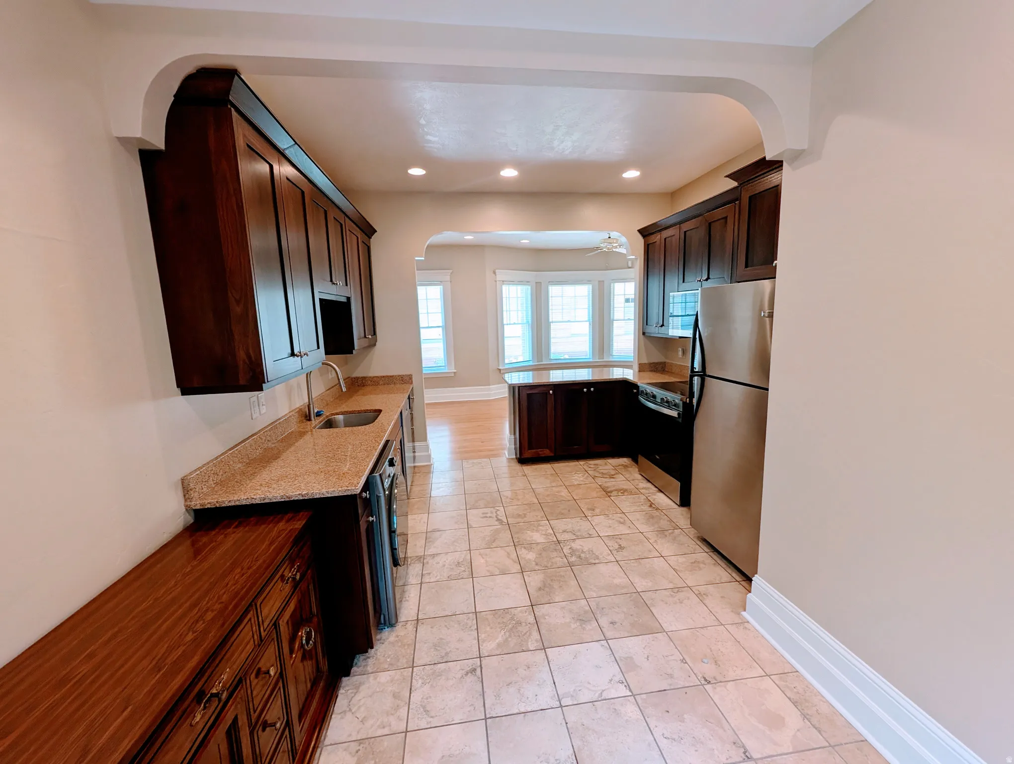 Kitchen featuring tile flooring, dark wood cabinetry, granite-style countertops, stainless steel appliances, and recessed lighting