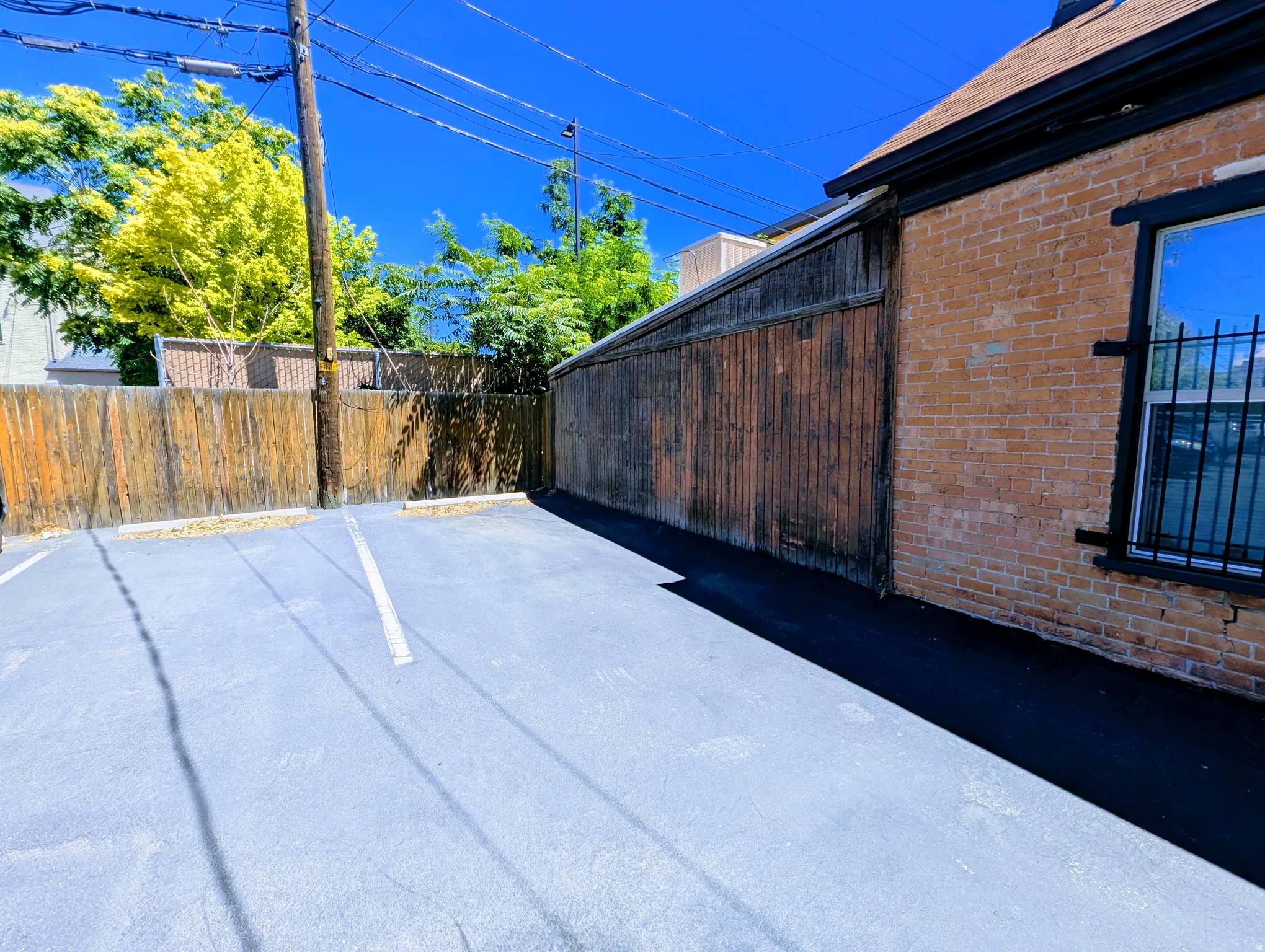 Paved parking area with marked spaces, bordered by a wooden privacy fence and a brick-faced structure