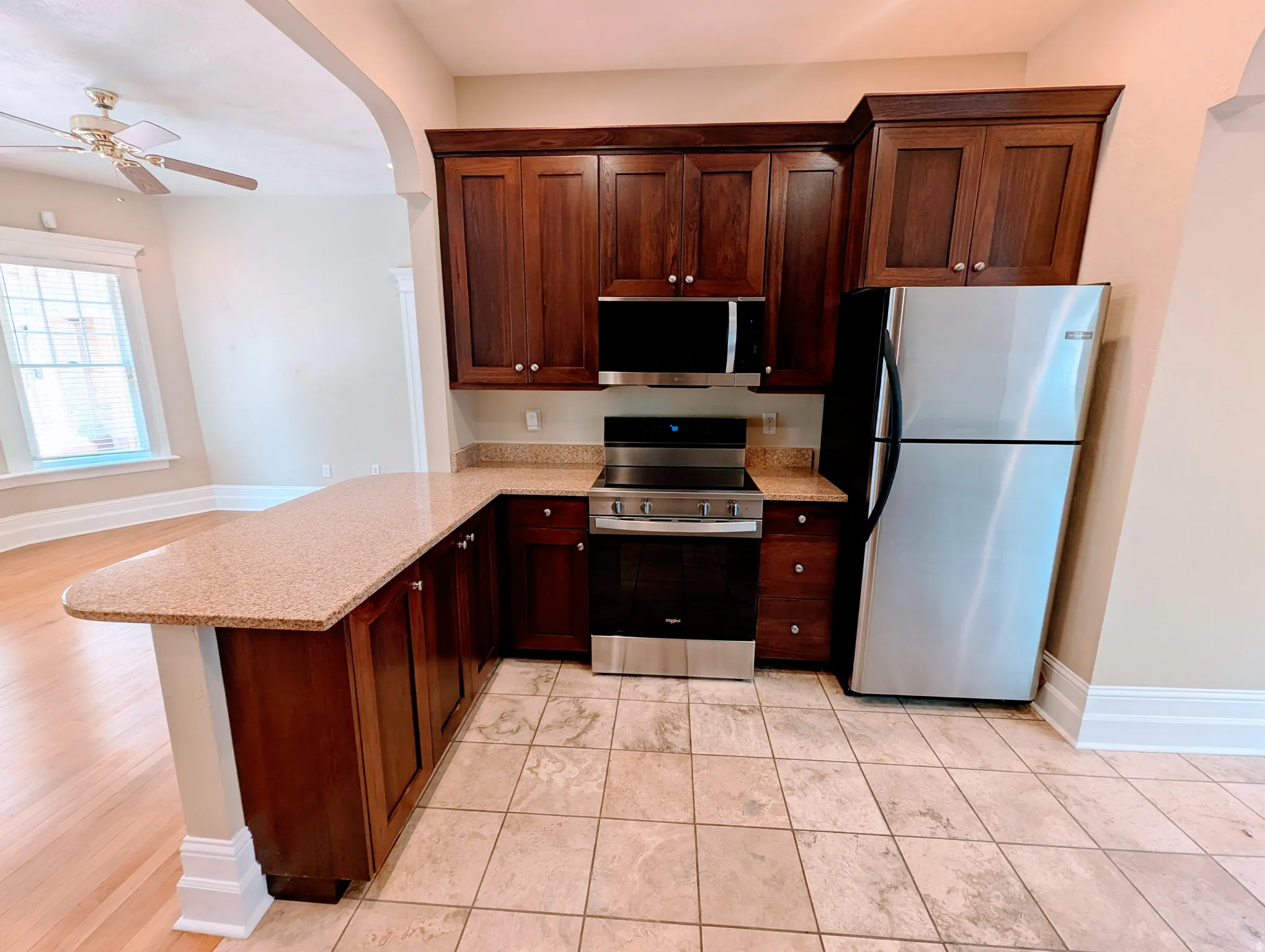 Kitchen featuring stainless steel appliances, wood-finish cabinetry, speckled countertops, and tiled flooring