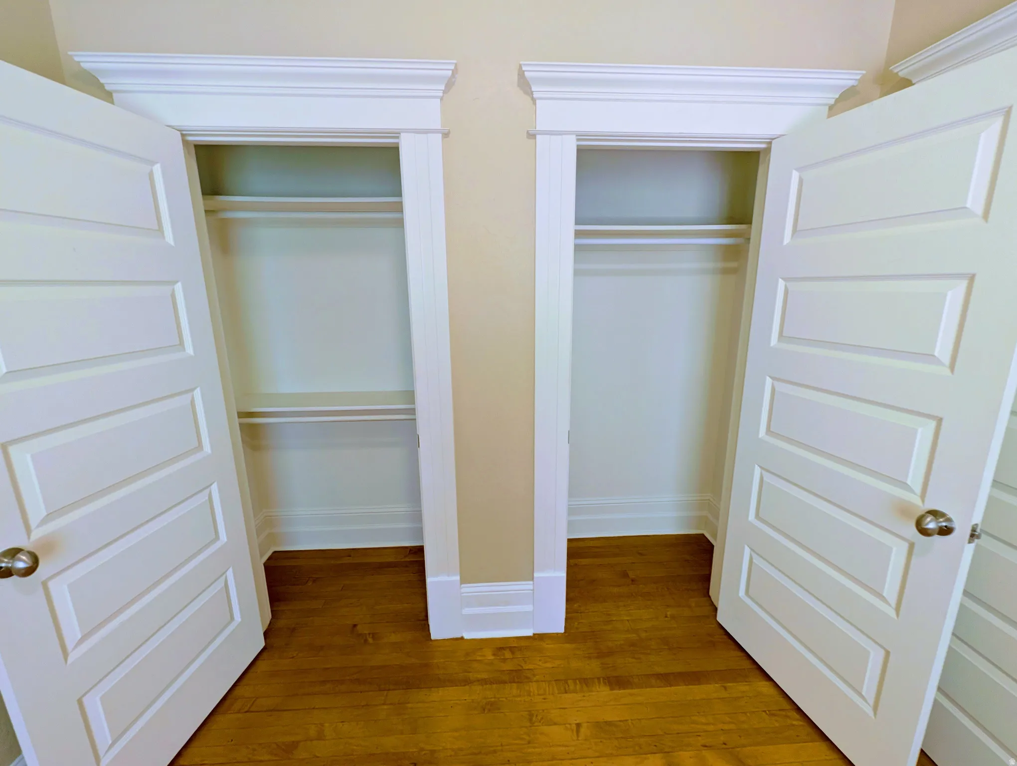 Twin closets featuring paneled doors, crown molding, and wood-finish flooring
