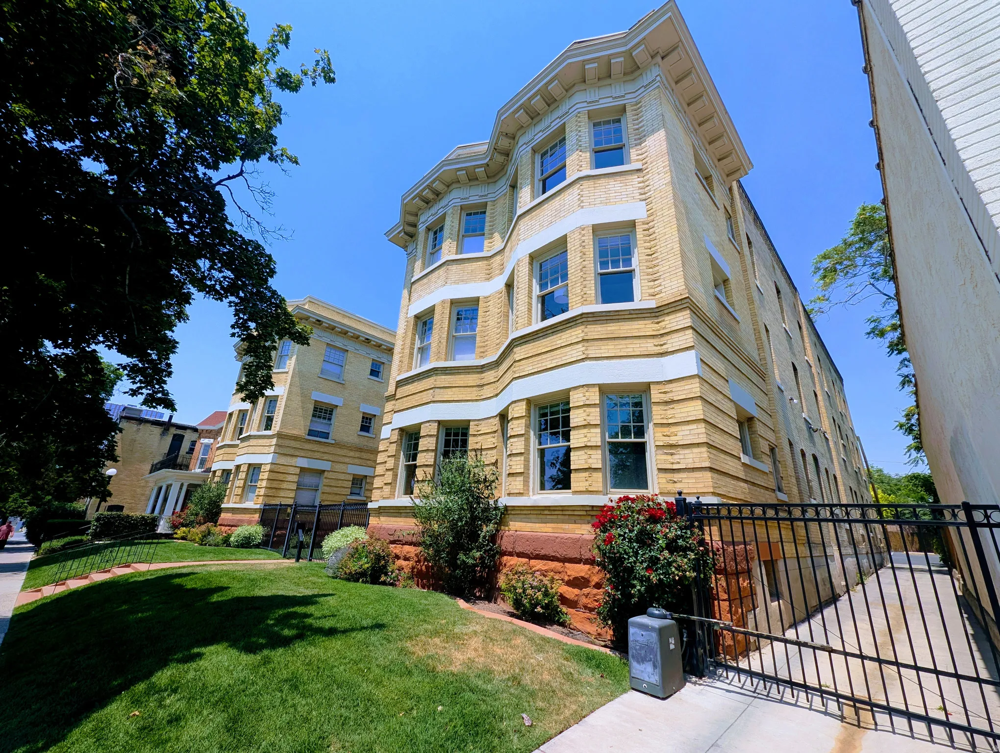 Multi-story brick facade building featuring bay windows, white trim accents, a decorative cornice, and a wrought iron fence