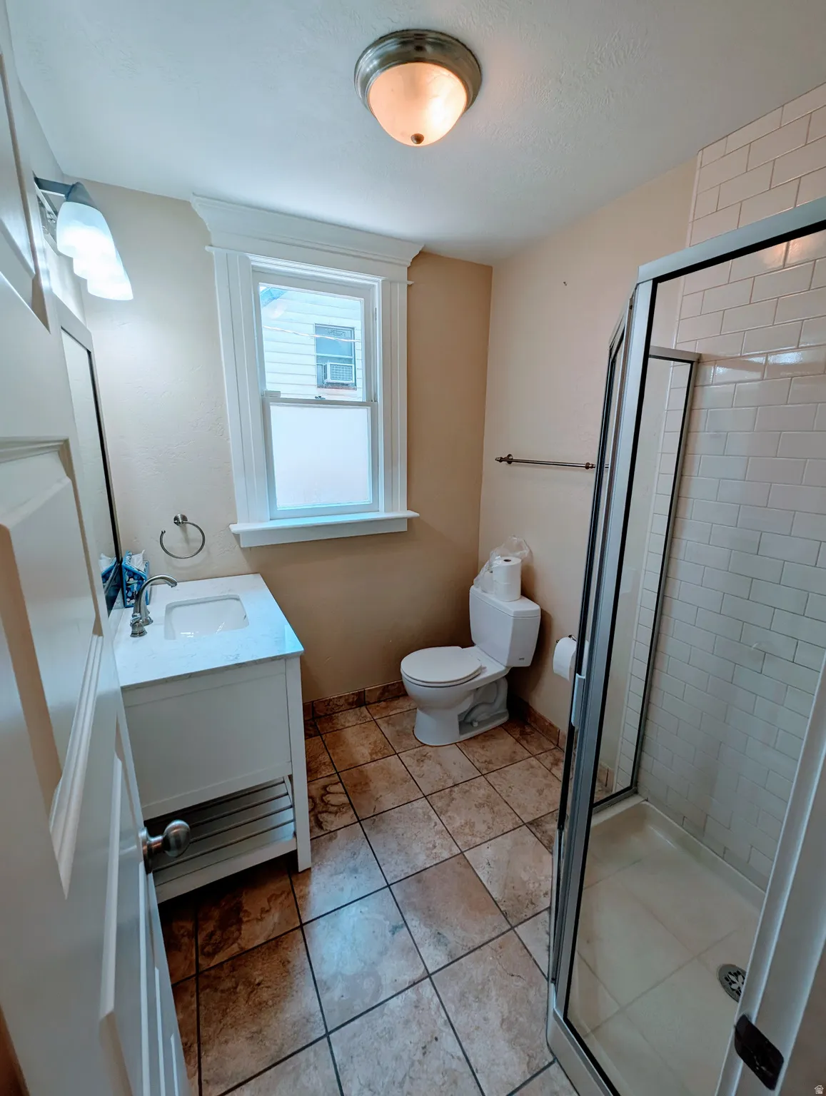 Bathroom featuring a glass-enclosed shower, subway tile shower surround, square tile flooring, single vanity with a white countertop and undermount sink, and a window with white trim