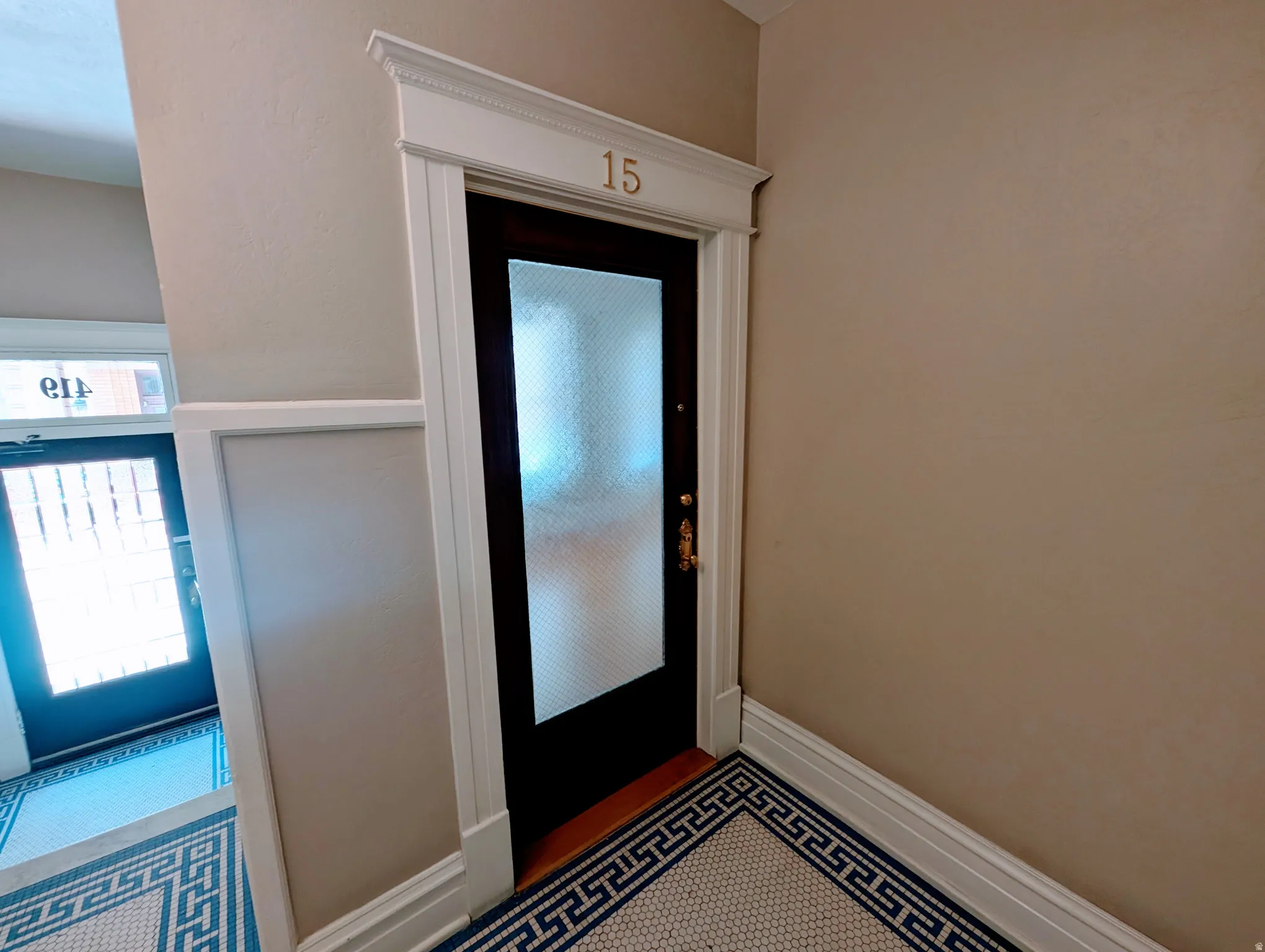 Entry door featuring a textured glass panel, decorative door trim with a number accent, and a brass door handle
