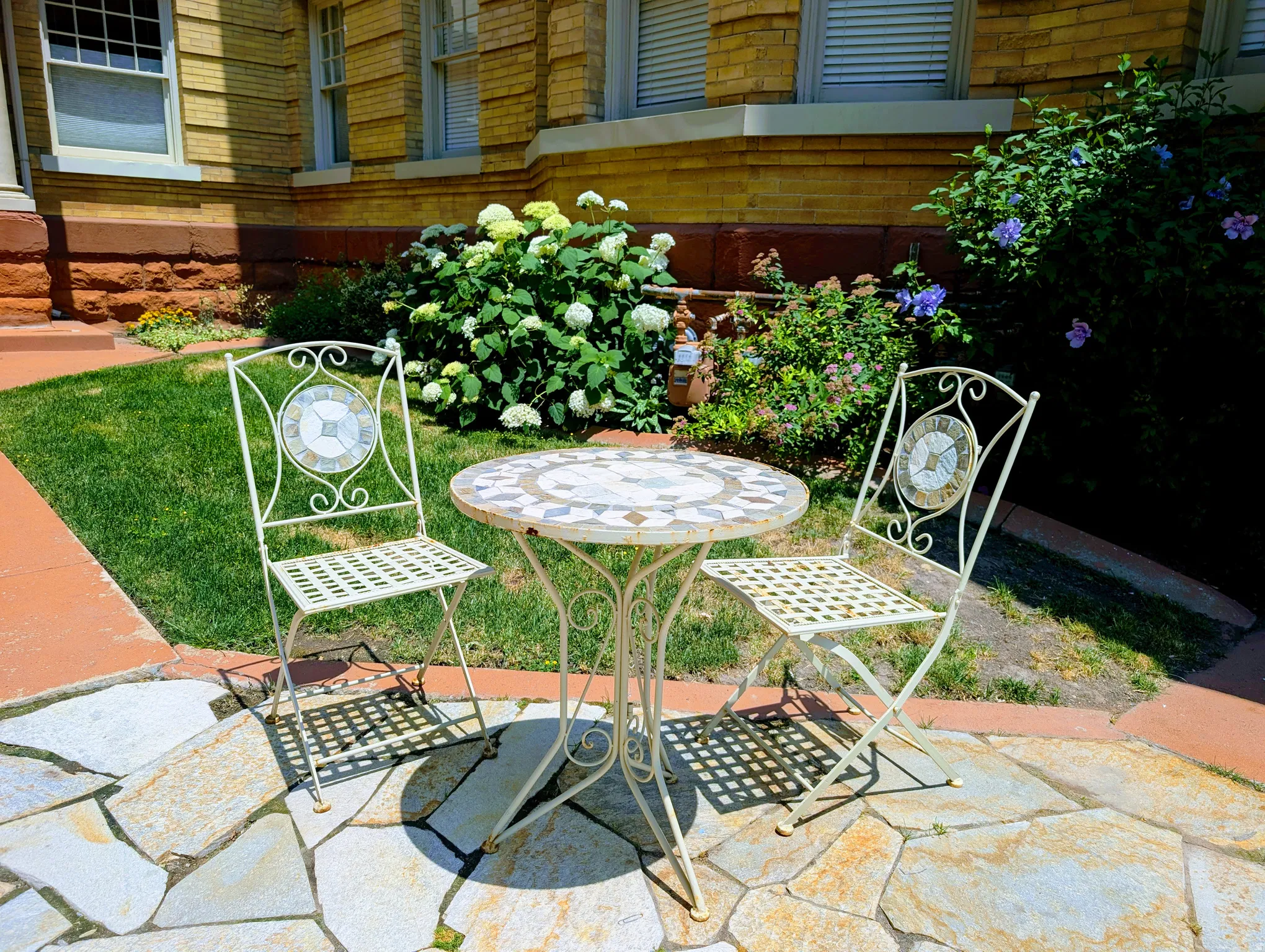 Flagstone patio area with a terracotta border, surrounded by manicured lawn and mature landscaping