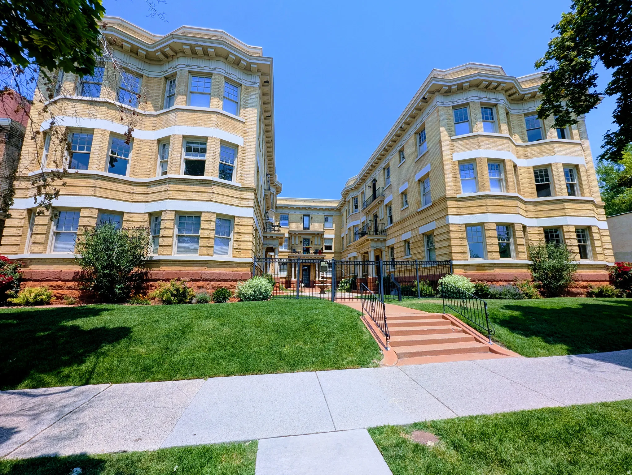 Multi-story brick building with ornate architectural details, featuring bay windows, decorative facade banding, and a prominent entryway with steps and iron railings