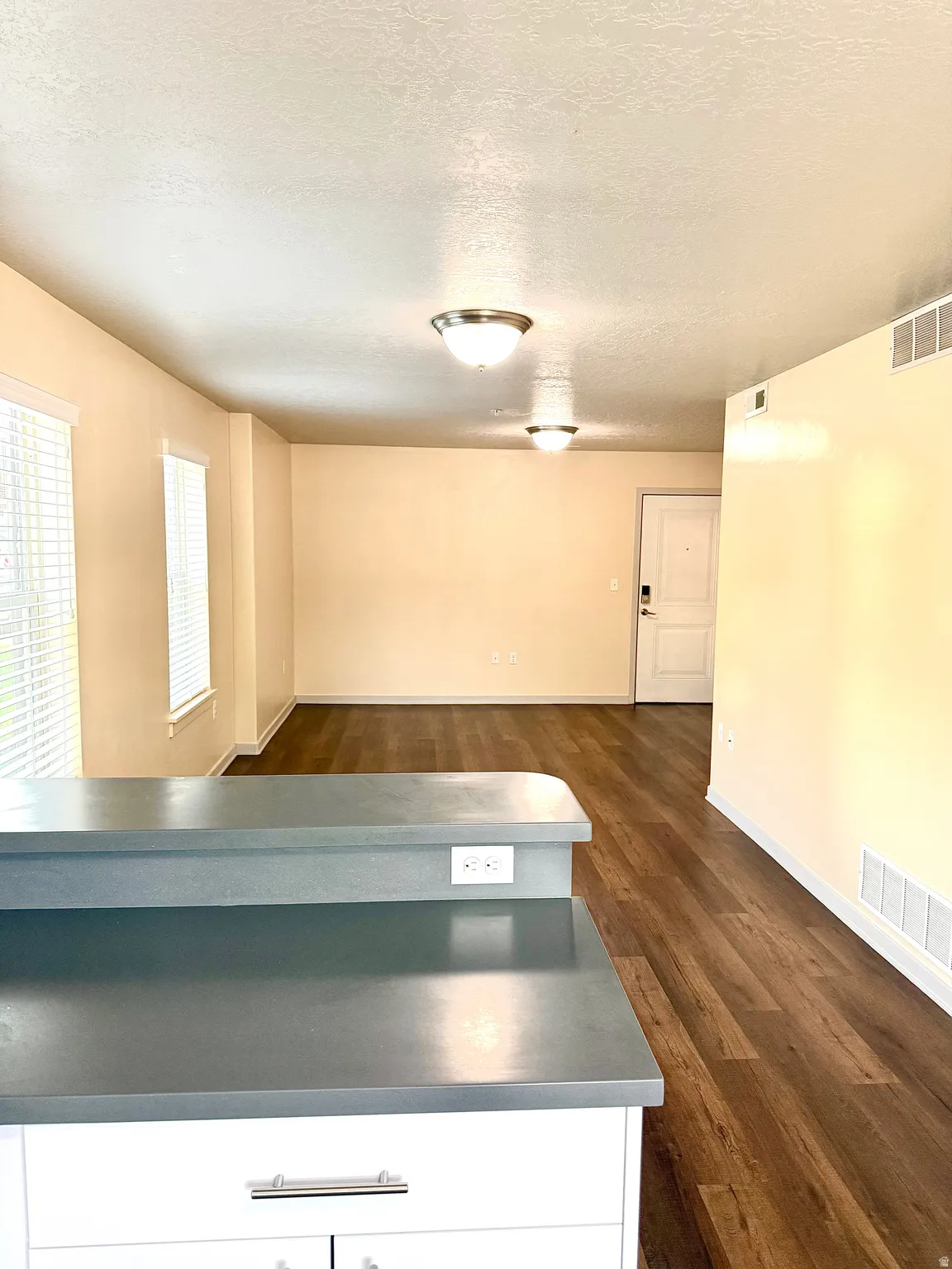 Kitchen island with a durable countertop, white cabinetry with silver hardware, and wood-finish flooring extending into the open space