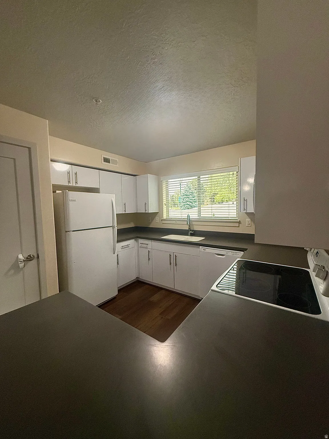 Kitchen featuring white cabinetry, dark countertops, wood-finish flooring, a white refrigerator, and a window with blinds