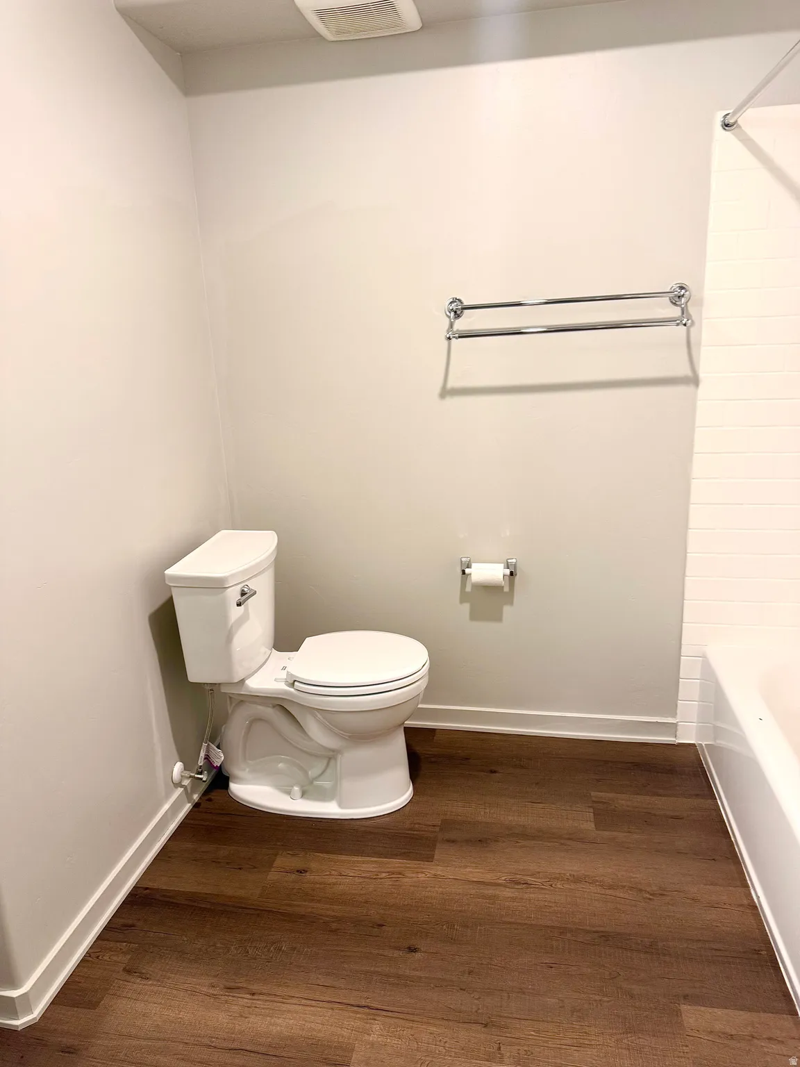 Bathroom featuring wood-finish flooring, a white toilet, and a bathtub with white subway tile surround