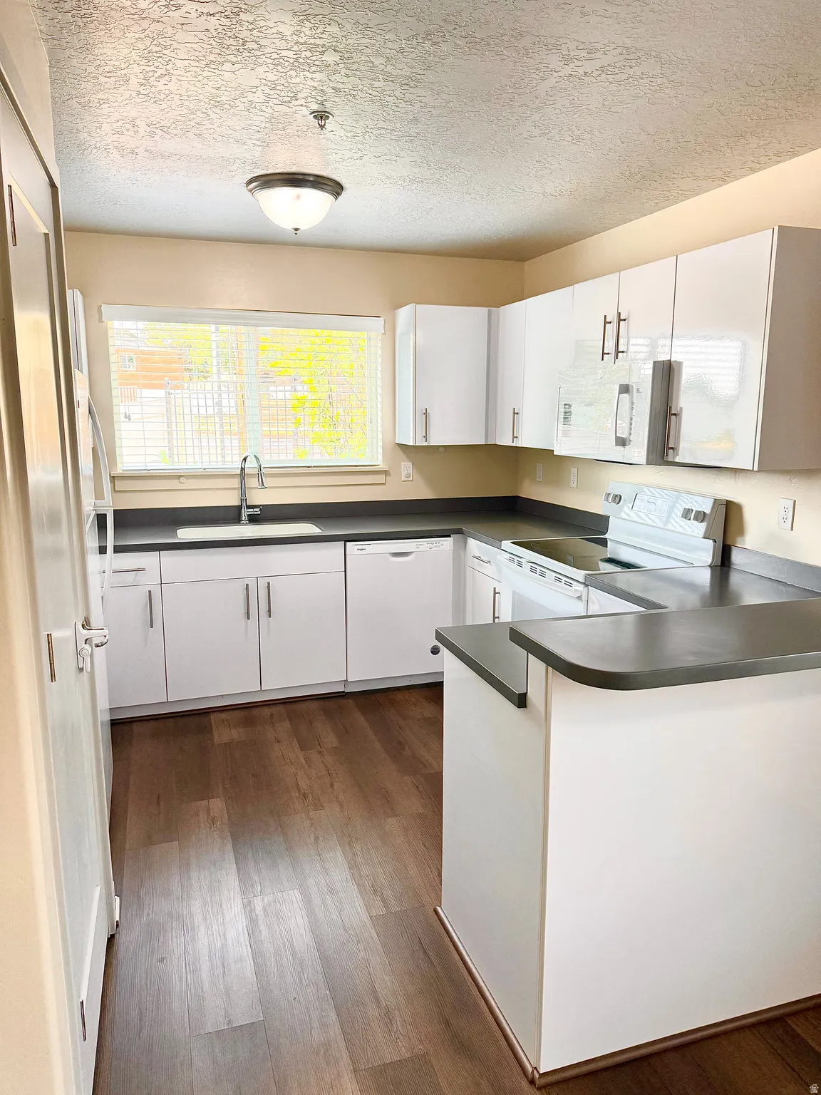 Kitchen featuring white cabinetry, dark countertops, wood-finish flooring, a stainless steel sink, and an electric range