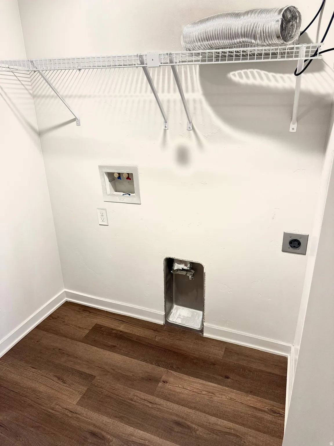 Dedicated laundry area featuring wood-finish flooring, white wire shelving, baseboard molding, appliance hookups, and a dryer vent