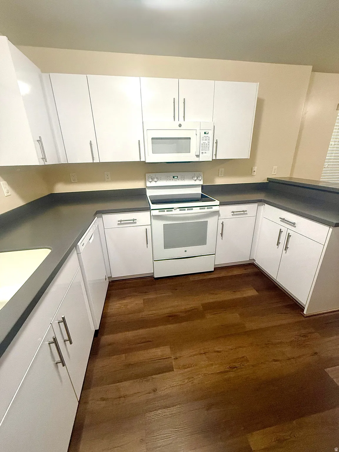 U-shaped kitchen featuring white cabinetry with silver hardware, dark countertops, and wood-finish flooring