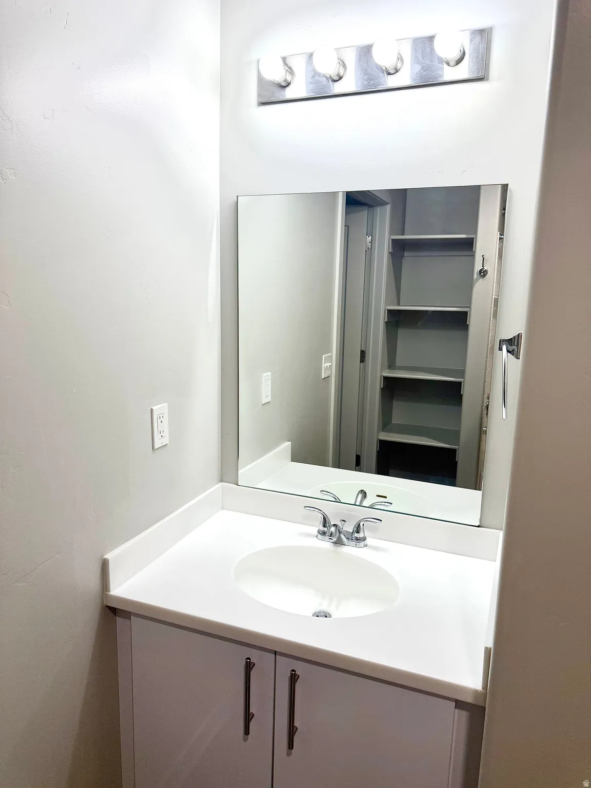 Vanity with a white countertop featuring an integrated oval sink, chrome faucet, and under-sink cabinetry