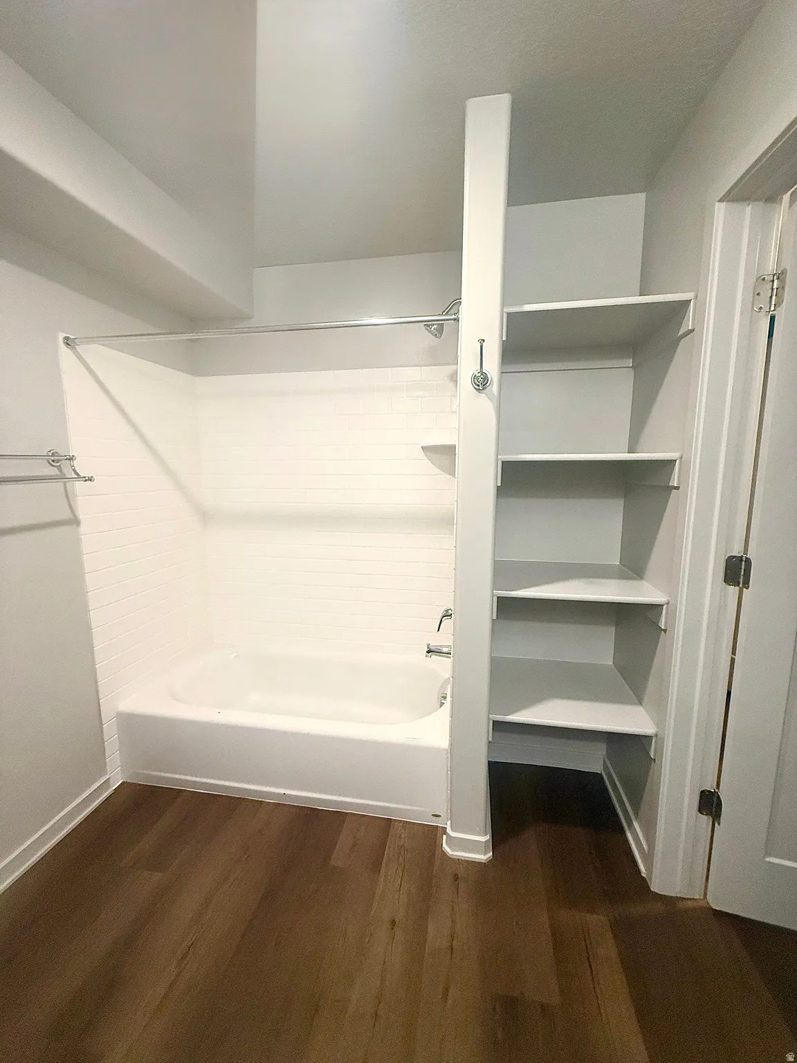Bathroom featuring a white bathtub, subway tile surround, wood-finish flooring, and built-in shelving