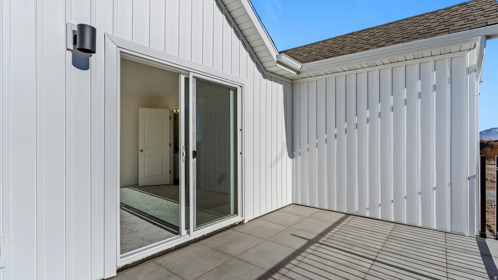 Exterior patio featuring white board and batten siding, dark gray paving stones, and a contemporary wall light fixture