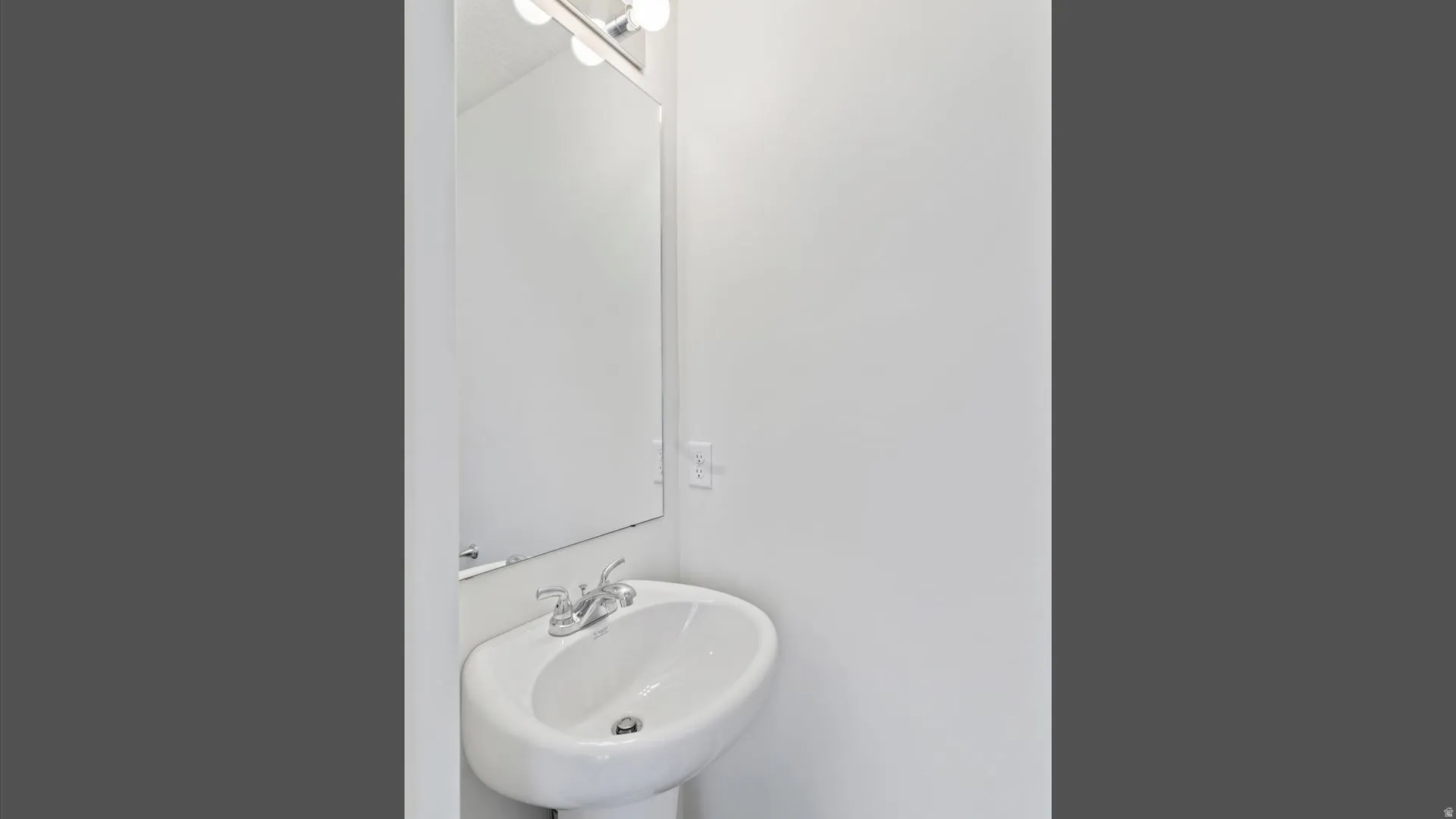 Pedestal sink with chrome faucet, large wall mirror, and modern vanity lighting