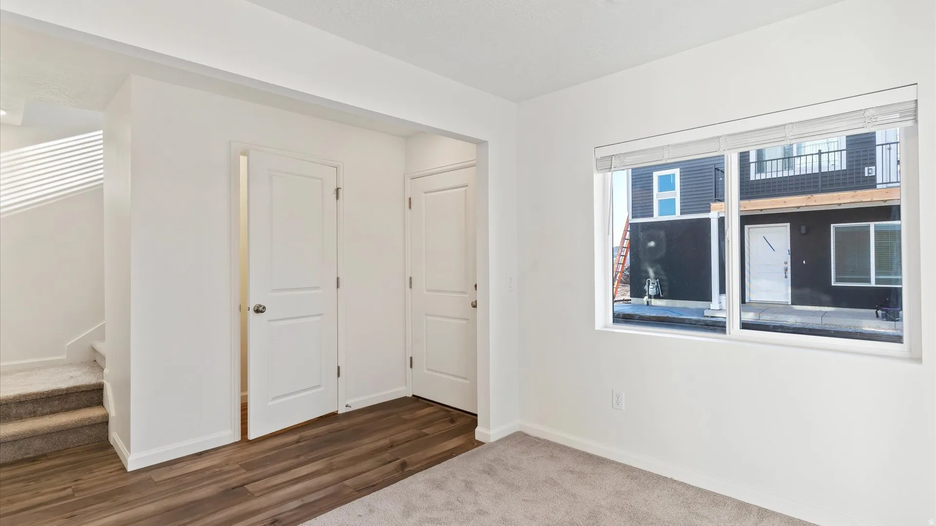 Room featuring a large window, light-toned carpeting, and wood-finish flooring
