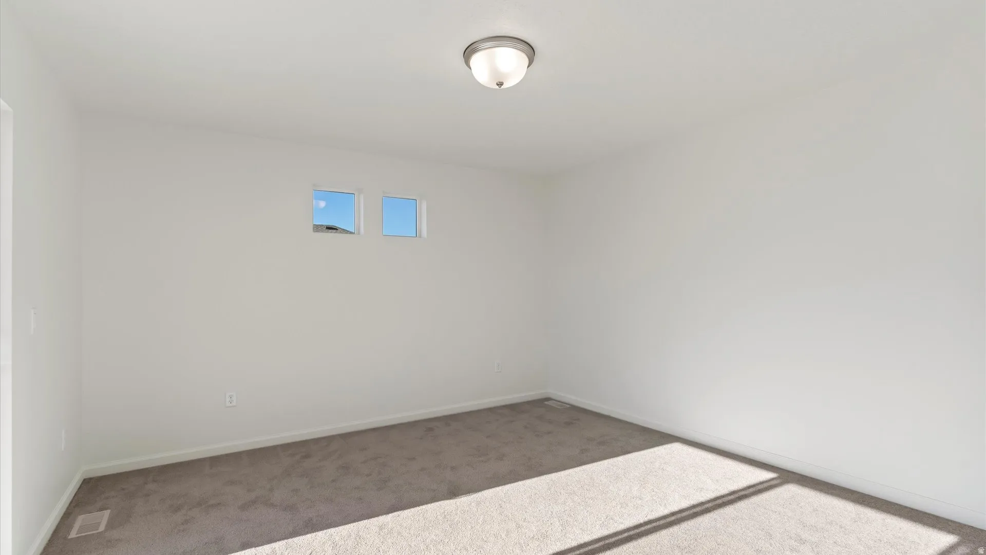 Neutral wall colors, plush carpet flooring, two upper-level windows, and a flush-mount ceiling light fixture