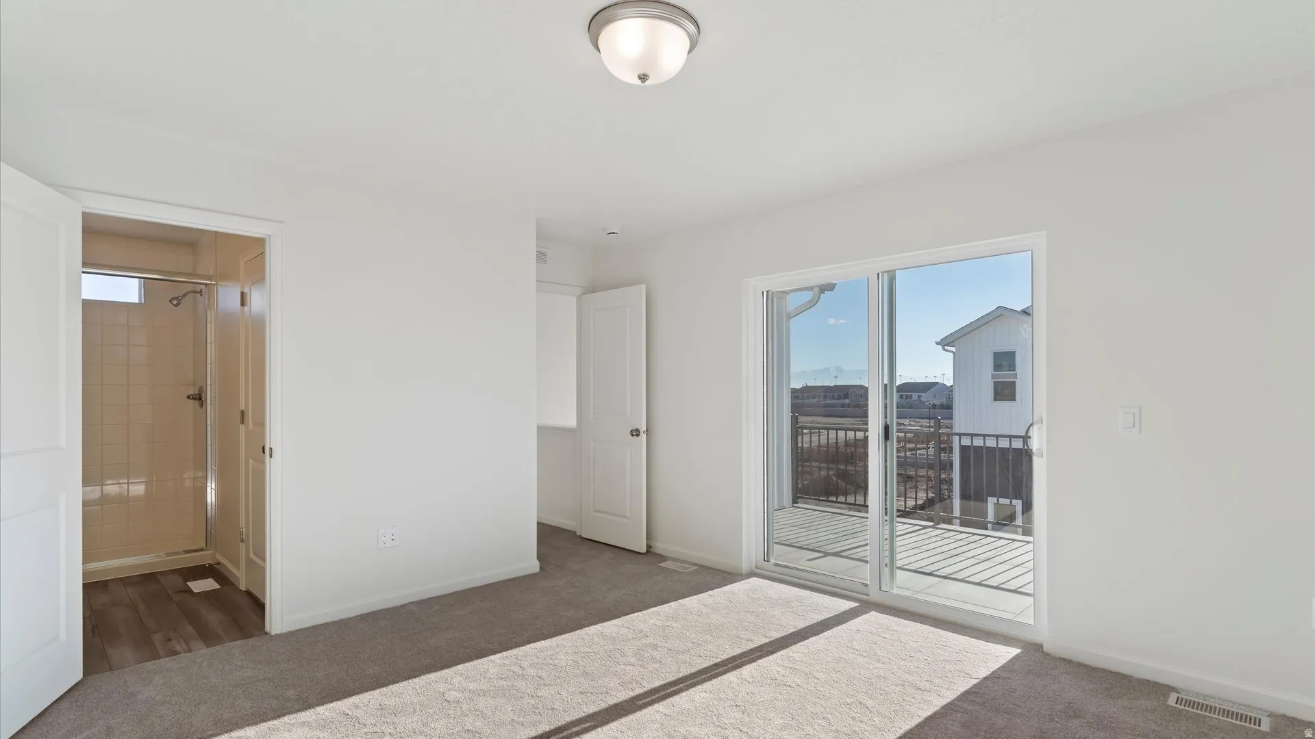 Bright room featuring neutral carpeting, white painted walls, a semi-flush mount ceiling light, and sliding glass doors opening to a private balcony