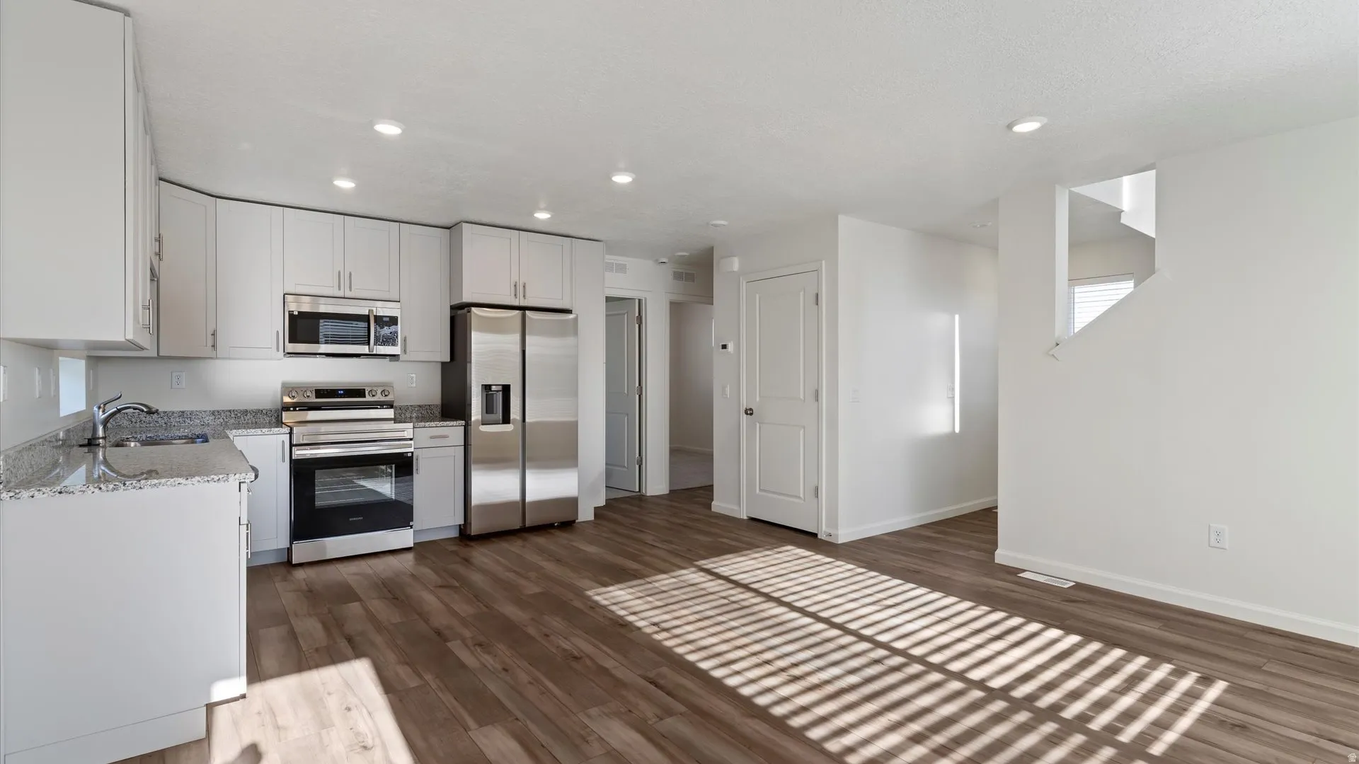 Kitchen featuring light gray cabinetry, stainless steel appliances, speckled countertops, and wood-finish flooring