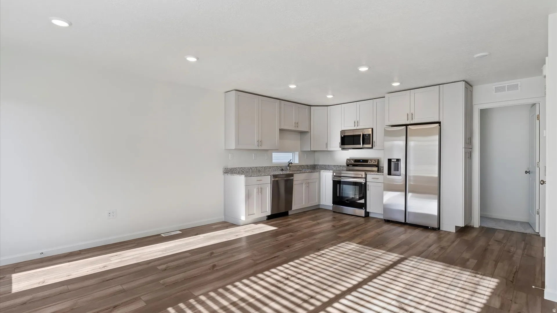 Open-concept kitchen featuring light wood-finish flooring, white cabinetry, stainless steel appliances, and recessed lighting