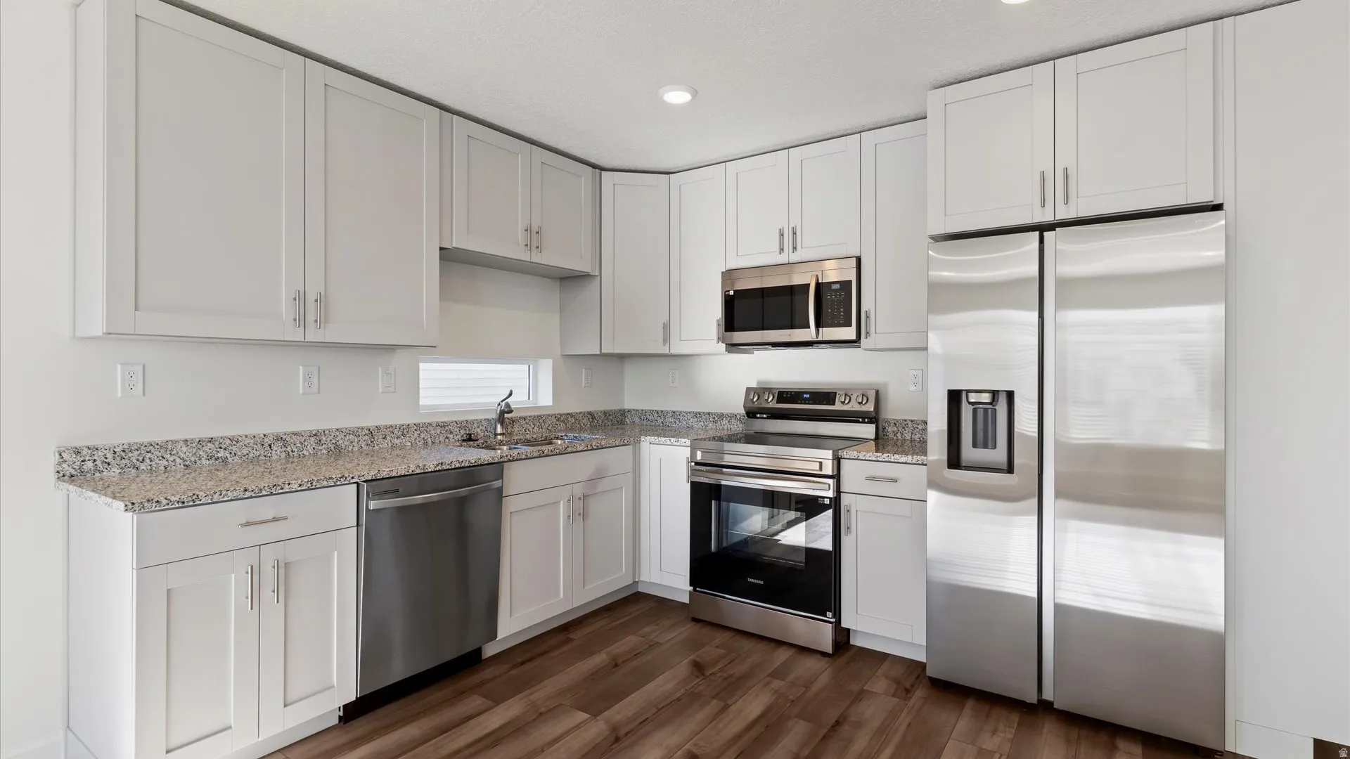 Modern kitchen featuring white shaker cabinetry, granite countertops, stainless steel appliances, wood-finish flooring, and recessed lighting