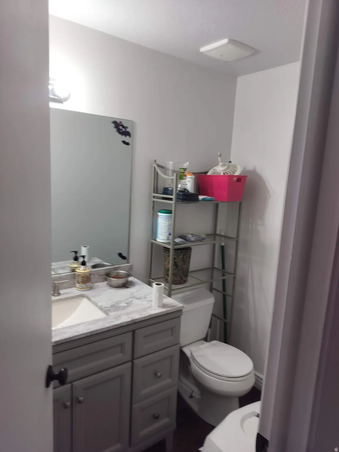 Bathroom featuring a gray vanity with a white countertop and integrated sink, a wall-mounted mirror, and a commode