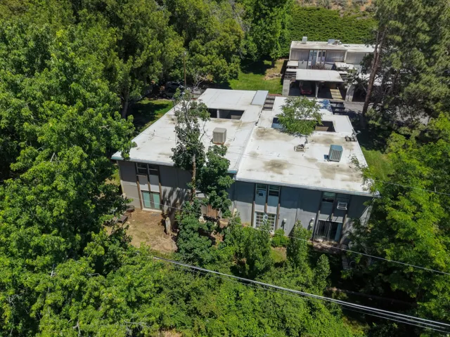 Multi-level structure featuring a flat roofline and grey facade, surrounded by mature trees